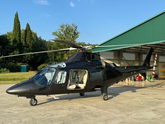 Black Agusta helicopter on a private helipad surrounded by Tuscan cypress trees